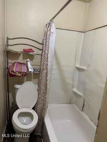 bathroom featuring toilet and shower / tub combo with curtain