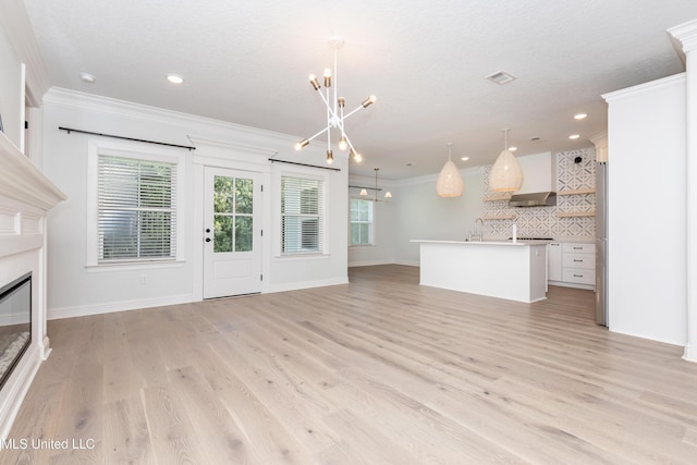 unfurnished living room featuring an inviting chandelier, crown molding, and light hardwood / wood-style floors