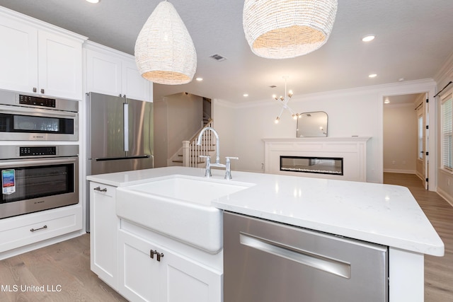 kitchen with sink, white cabinets, hanging light fixtures, a kitchen island with sink, and stainless steel appliances