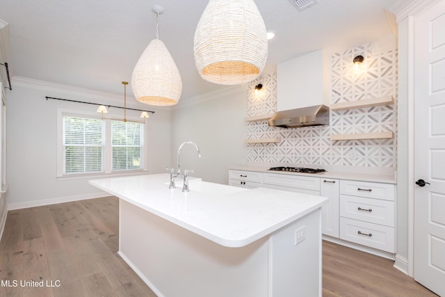 kitchen with sink, extractor fan, an island with sink, white cabinets, and stainless steel gas stovetop