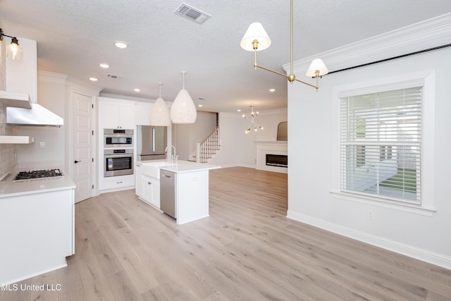 kitchen with white cabinetry, appliances with stainless steel finishes, decorative light fixtures, and an island with sink