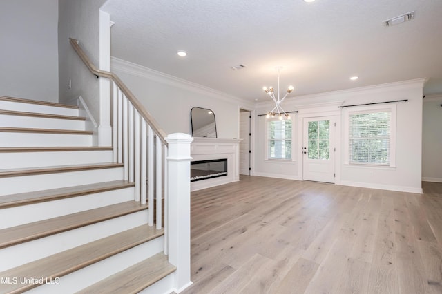 unfurnished living room featuring crown molding, a chandelier, and light hardwood / wood-style floors