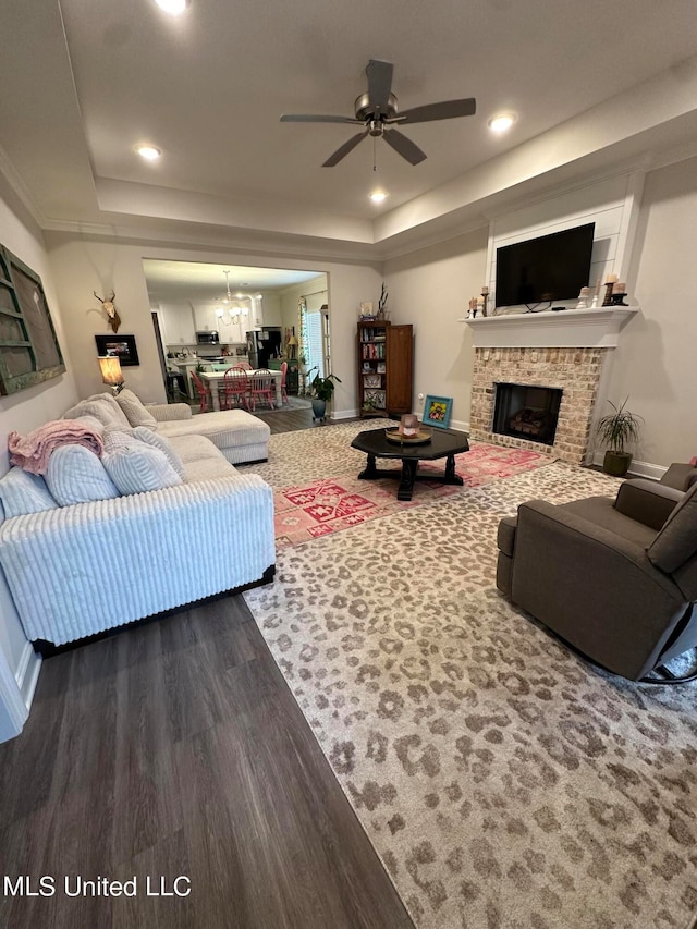 living room with a tray ceiling, wood-type flooring, a fireplace, and ceiling fan