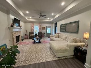 living room with a fireplace, a tray ceiling, wood-type flooring, and ceiling fan