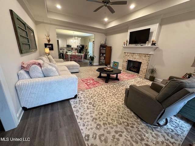 living room with hardwood / wood-style flooring, ceiling fan with notable chandelier, and a raised ceiling