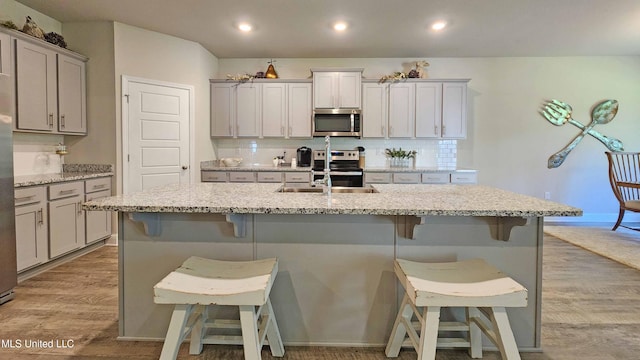 kitchen with a kitchen bar, appliances with stainless steel finishes, light hardwood / wood-style flooring, and an island with sink