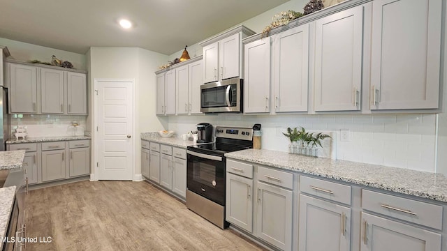 kitchen with light stone countertops, appliances with stainless steel finishes, backsplash, gray cabinetry, and light hardwood / wood-style flooring