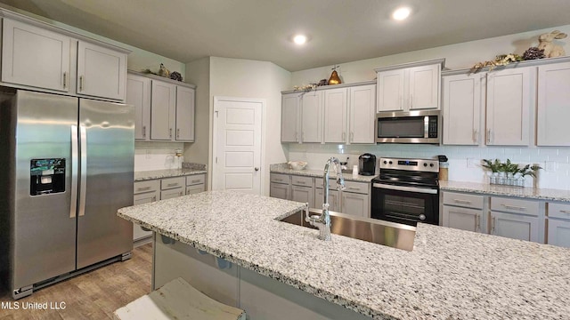 kitchen featuring light stone counters, sink, appliances with stainless steel finishes, and light hardwood / wood-style flooring