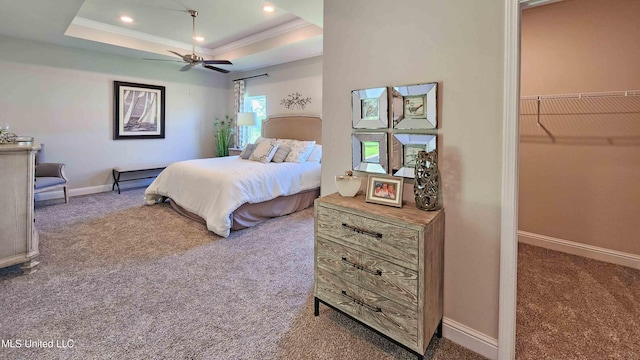 carpeted bedroom featuring a spacious closet, a raised ceiling, ceiling fan, and ornamental molding