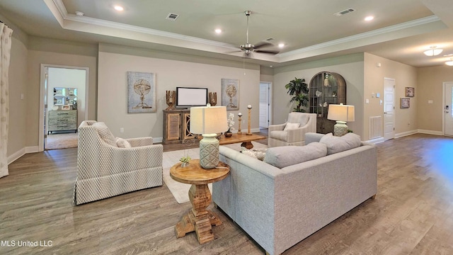 living room with ceiling fan, wood-type flooring, crown molding, and a tray ceiling