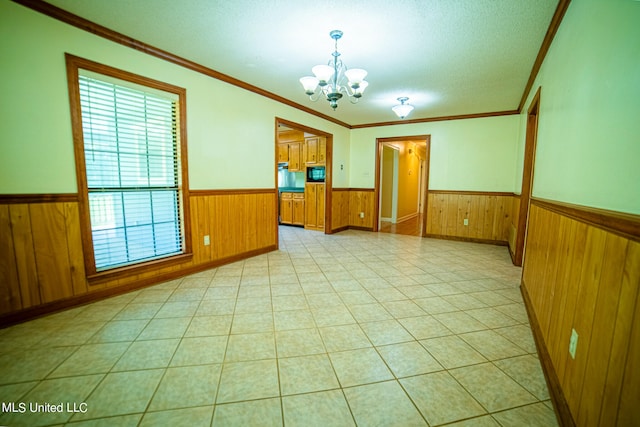 empty room featuring crown molding, a textured ceiling, an inviting chandelier, and wooden walls