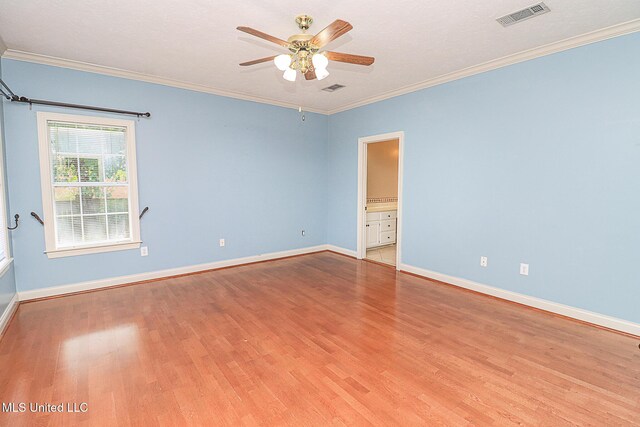 empty room with ceiling fan, visible vents, wood finished floors, baseboards, and ornamental molding
