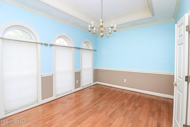 empty room with an inviting chandelier, baseboards, wood finished floors, a tray ceiling, and ornamental molding
