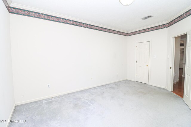 carpeted spare room featuring crown molding, baseboards, and visible vents