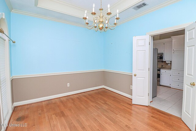 unfurnished dining area with visible vents, crown molding, a raised ceiling, light wood-style flooring, and a notable chandelier