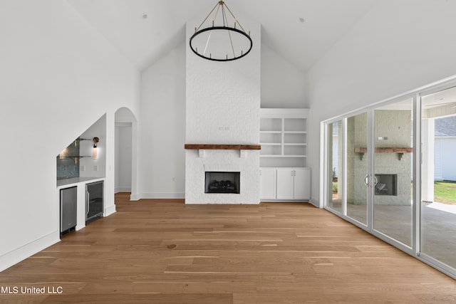 unfurnished living room featuring high vaulted ceiling, built in shelves, a fireplace, and hardwood / wood-style floors