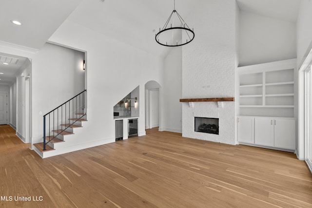 unfurnished living room featuring light hardwood / wood-style floors, a high ceiling, a stone fireplace, and built in features