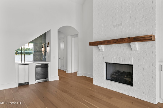 bar featuring a towering ceiling, a fireplace, stainless steel fridge, hardwood / wood-style floors, and beverage cooler