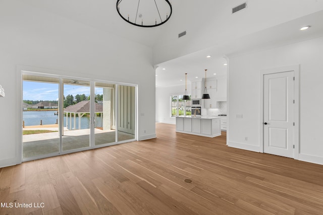 unfurnished living room featuring a water view, light hardwood / wood-style floors, and high vaulted ceiling