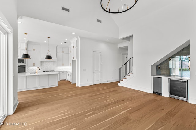 unfurnished living room featuring wine cooler, high vaulted ceiling, sink, and light wood-type flooring