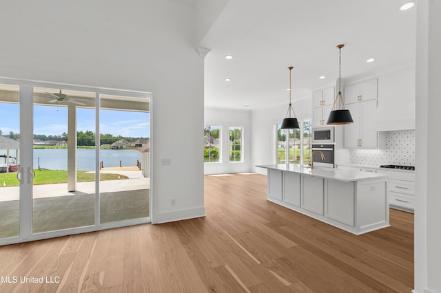 kitchen featuring oven, white microwave, white cabinetry, light hardwood / wood-style floors, and a water view