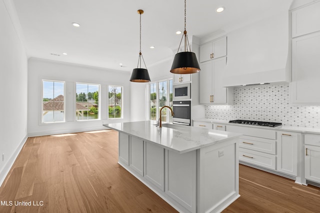 kitchen with a kitchen island with sink, stainless steel gas cooktop, light wood-type flooring, white cabinets, and light stone counters