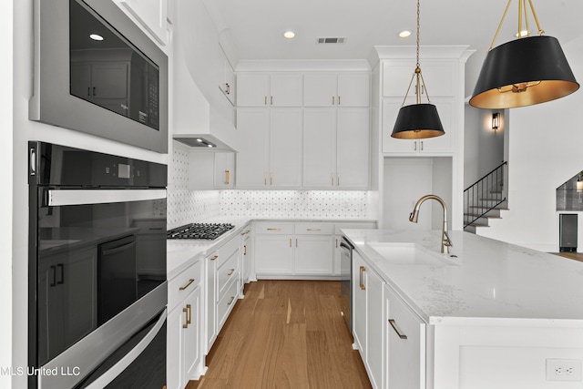 kitchen with white cabinets, a center island with sink, light stone counters, appliances with stainless steel finishes, and sink