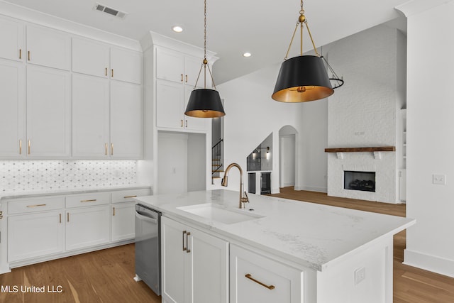 kitchen featuring dishwasher, an island with sink, hanging light fixtures, sink, and light stone countertops