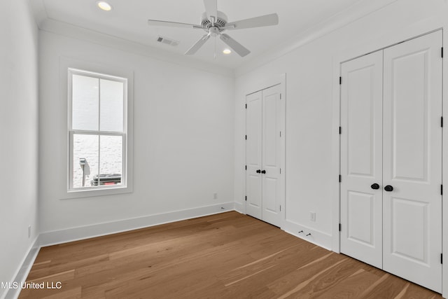 unfurnished bedroom featuring ornamental molding, two closets, wood-type flooring, and ceiling fan