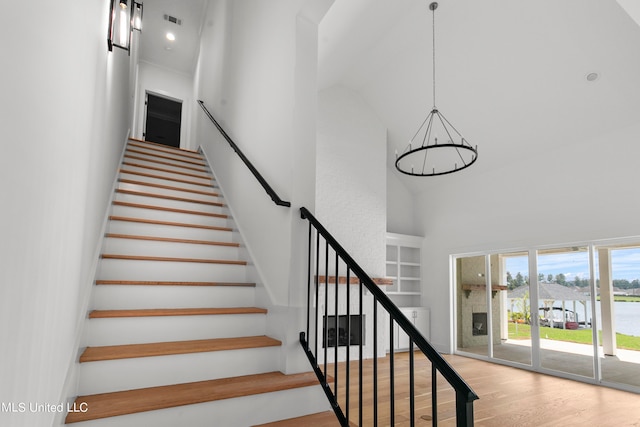 stairway with a chandelier, wood-type flooring, and a high ceiling