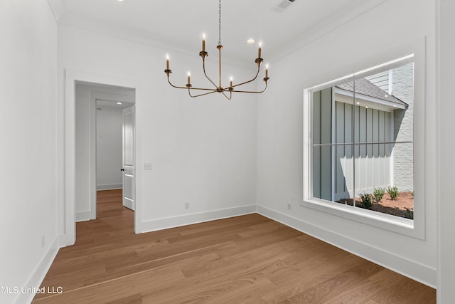 spare room featuring a notable chandelier, ornamental molding, and light wood-type flooring