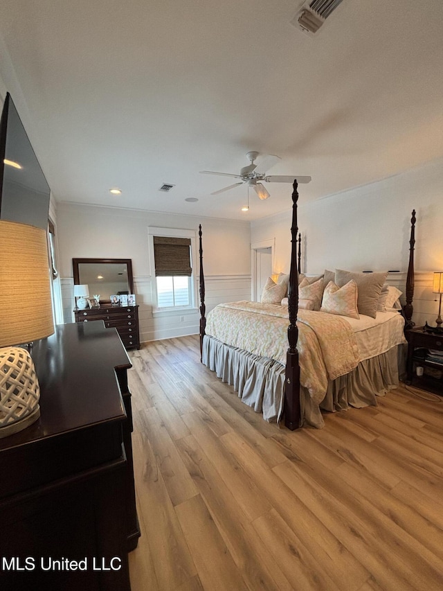 bedroom featuring a ceiling fan, a wainscoted wall, visible vents, and wood finished floors