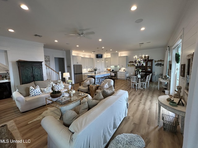 living area with light wood-type flooring, ceiling fan with notable chandelier, visible vents, and recessed lighting