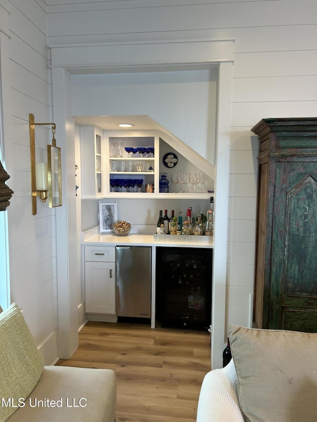 bar with light wood-type flooring, refrigerator, beverage cooler, and a dry bar