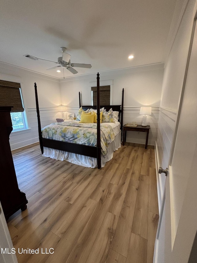 bedroom with ornamental molding, wainscoting, visible vents, and light wood finished floors