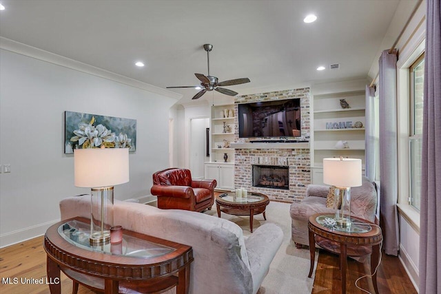 living room with ceiling fan, wood-type flooring, built in features, a fireplace, and crown molding