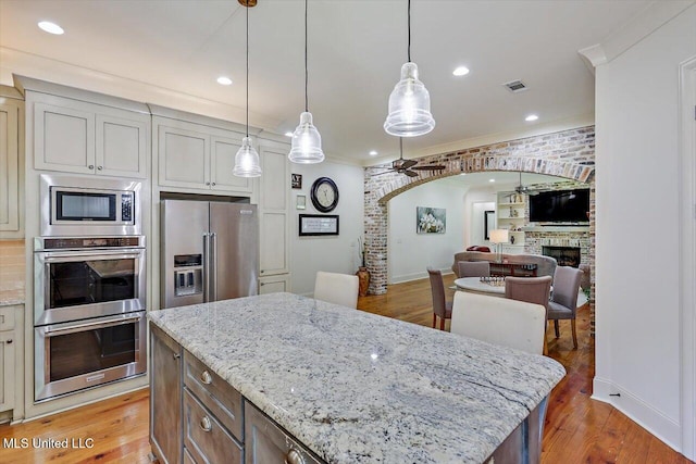 kitchen with appliances with stainless steel finishes, a kitchen island, light hardwood / wood-style floors, ceiling fan, and pendant lighting