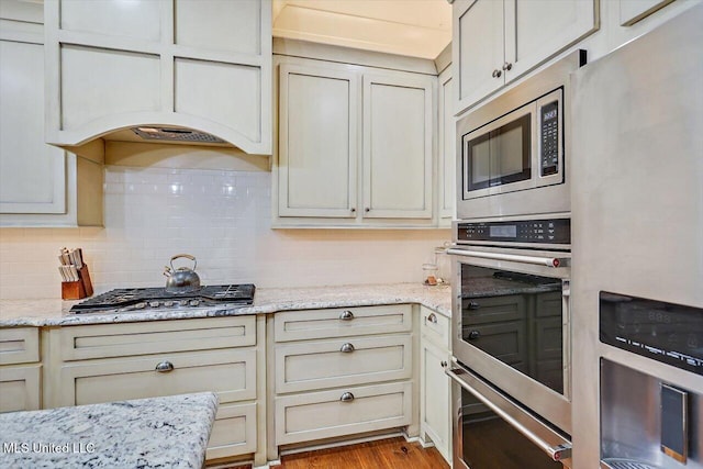 kitchen featuring decorative backsplash, cream cabinets, light stone countertops, light wood-type flooring, and stainless steel appliances