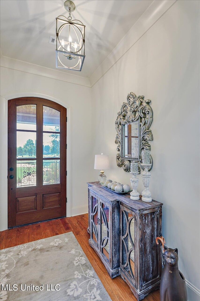 foyer entrance with ornamental molding, a chandelier, and hardwood / wood-style flooring