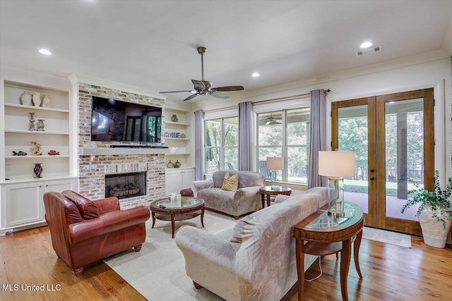 living room with light wood-type flooring, a fireplace, french doors, ceiling fan, and crown molding