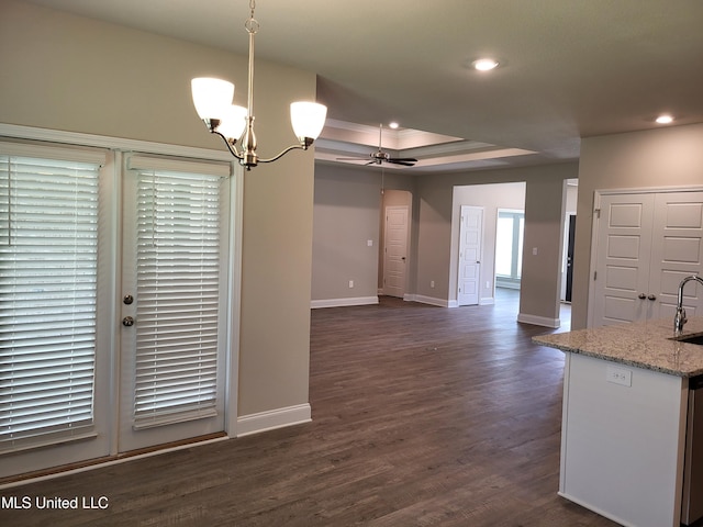 unfurnished dining area featuring ceiling fan with notable chandelier, dark hardwood / wood-style flooring, sink, and a tray ceiling