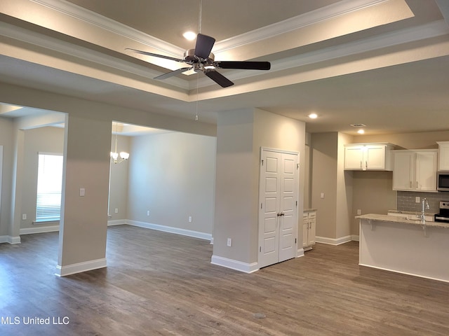 unfurnished living room featuring a tray ceiling, crown molding, dark hardwood / wood-style flooring, and ceiling fan with notable chandelier