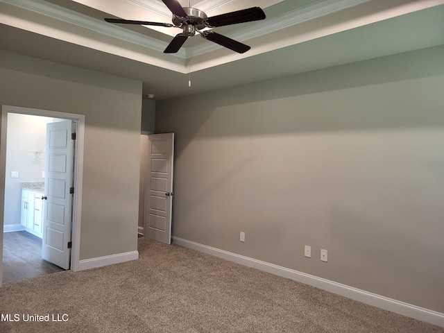 unfurnished bedroom with connected bathroom, ceiling fan, crown molding, a tray ceiling, and carpet