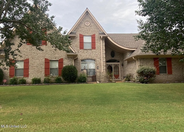 view of front of property featuring a front lawn, a shingled roof, and brick siding