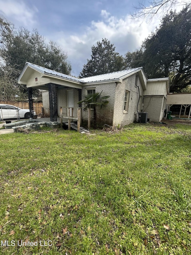 rear view of property with cooling unit, brick siding, a yard, and metal roof