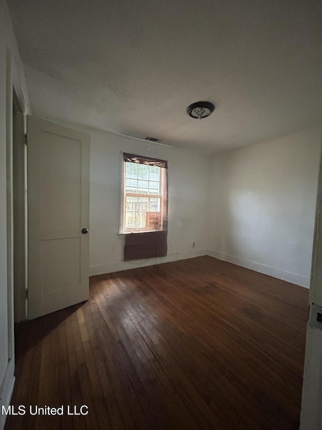 unfurnished room featuring dark wood-style floors, visible vents, and baseboards