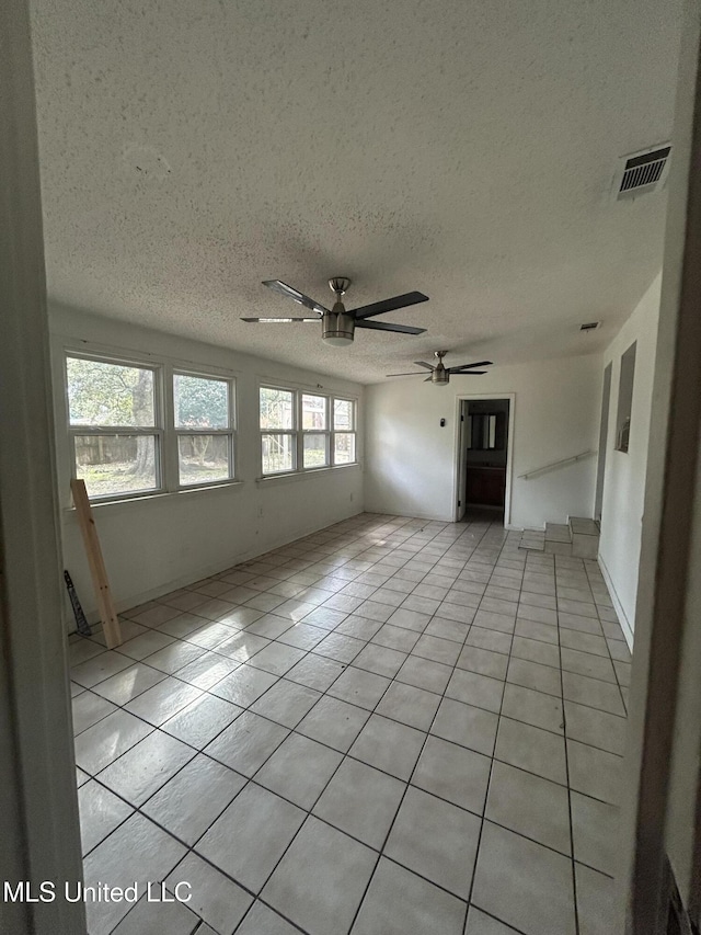 unfurnished room with a textured ceiling, light tile patterned floors, visible vents, and ceiling fan