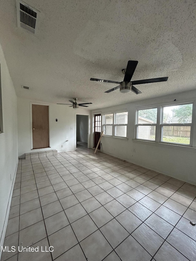 tiled empty room with visible vents, a textured ceiling, and ceiling fan