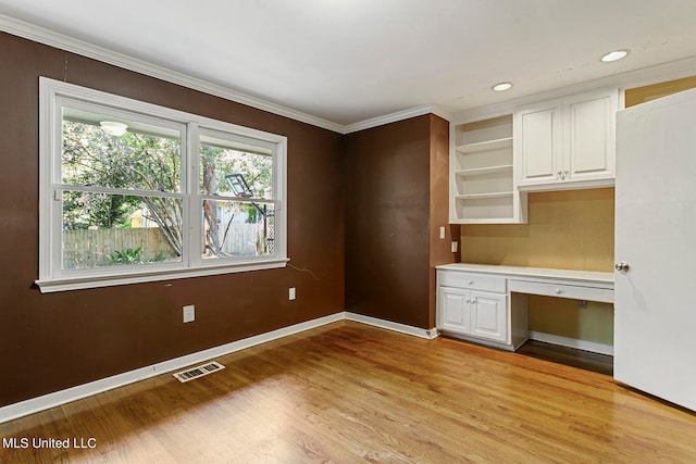 interior space featuring built in desk, crown molding, light wood-type flooring, and white cabinets