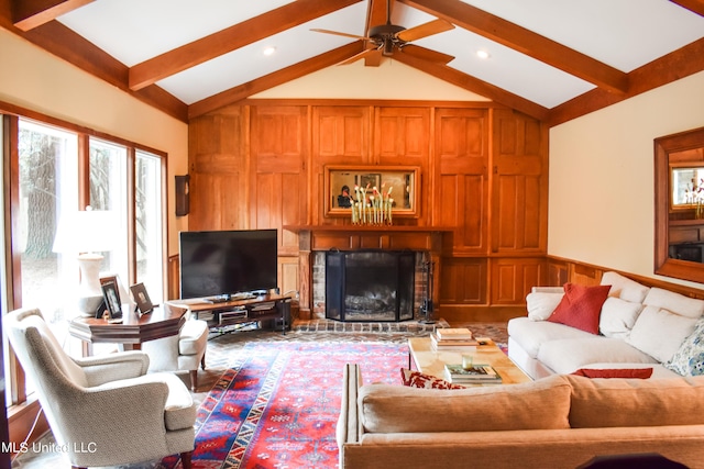 living room with ceiling fan, plenty of natural light, a brick fireplace, and vaulted ceiling with beams